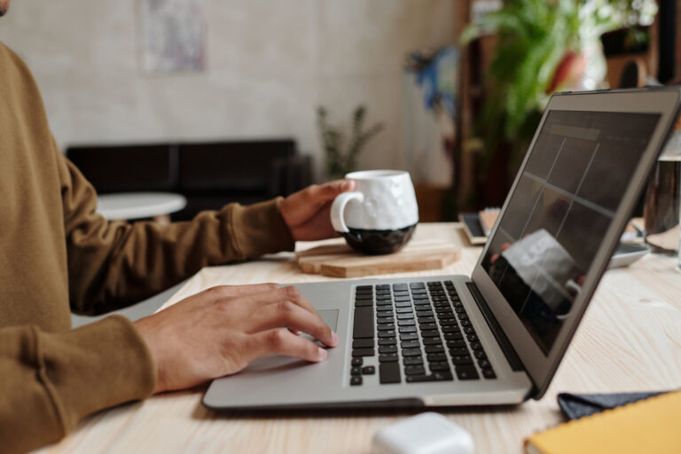 Close-up of a person using a laptop with a coffee mug on a wooden table