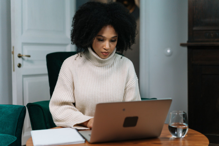 A woman in a cozy sweater works remotely at home with a laptop, appearing focused and productive.